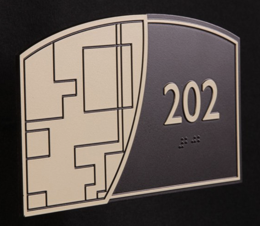 Tactile sign with intricate raised decorative elements, adding artistic patterns alongside functional text and braille.