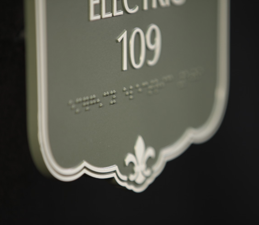Tactile sign with custom borders and shapes featuring raised text, Braille, and decorative elements in a seamless design.