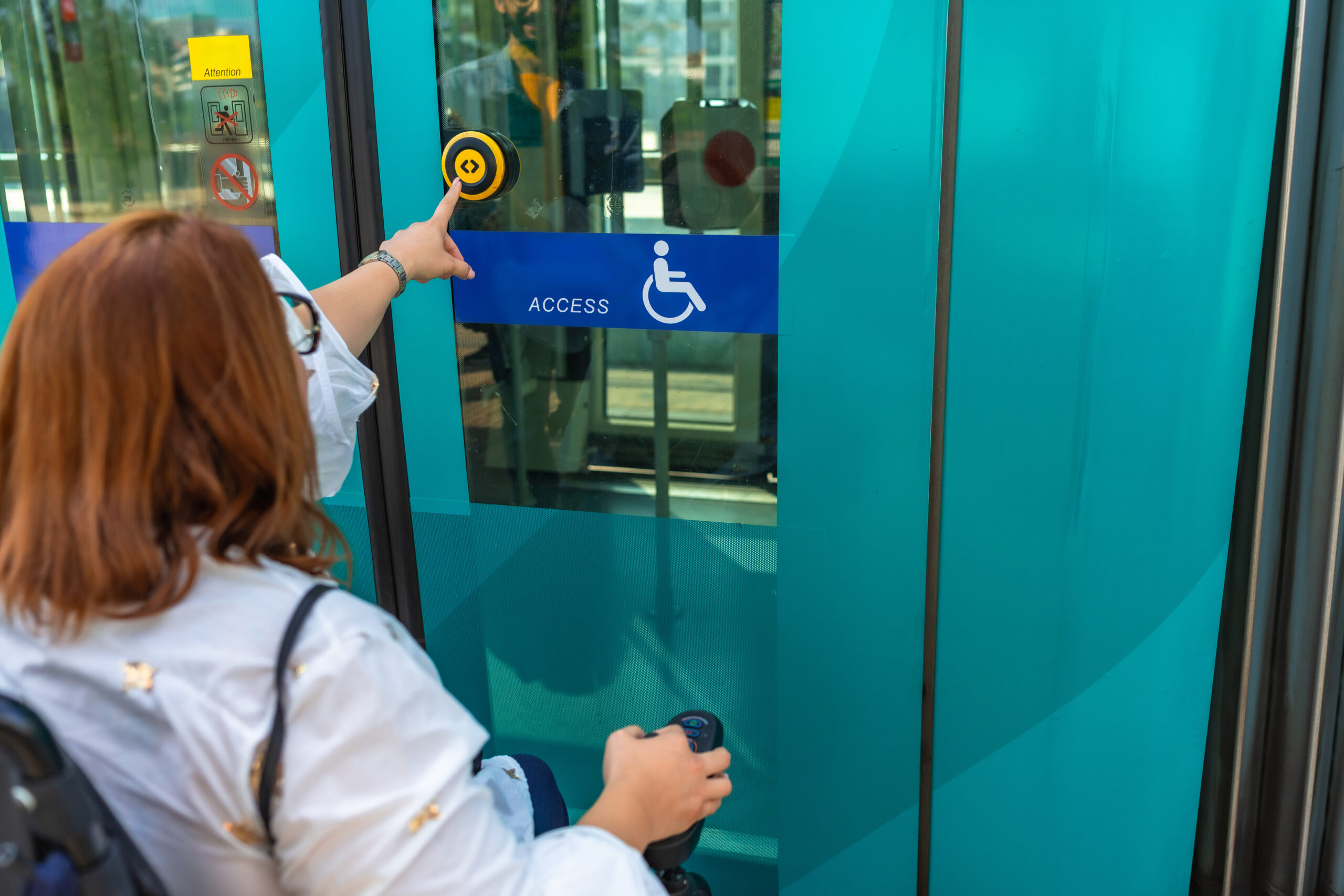 UV resistant photopolymer signs installed outdoors, and a woman in a wheelchair pushing a button to open a door.